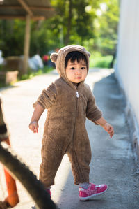 Portrait of cute baby girl wearing bear suit on footpath
