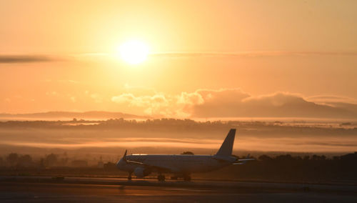 Airplane on runway against sky during sunset