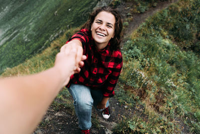 A young woman holds her partner's hand while climbing to the top of the mountain.