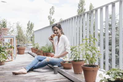 Smiling woman eating croissant with jam on balcony