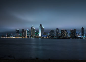 Sea by illuminated buildings against sky at night