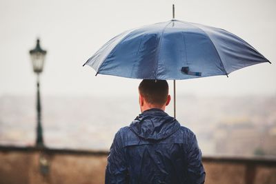 Rear view of man with umbrella walking on street during rainy season
