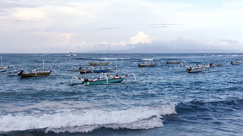 Outrigger boats in sea against cloudy sky