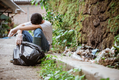 Tired man with garbage bag sitting roadside