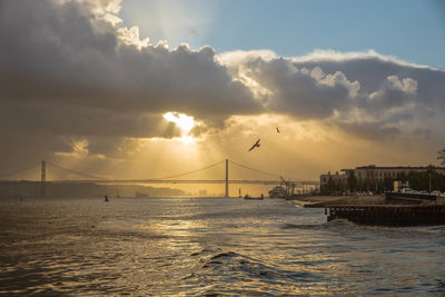 Suspension bridge over sea against sky during sunset, lisbon, portugal.