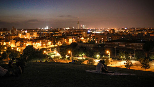 Rear view of couple embracing at park against illuminated cityscape