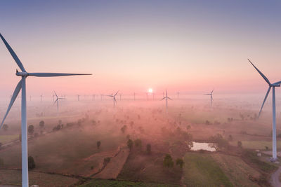 Windmills on landscape against sky during sunset