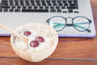 High angle view of milk with plum and banana in wooden bowl against laptop