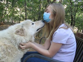 Full length of woman sitting with timber wolf in wolf sanctuary