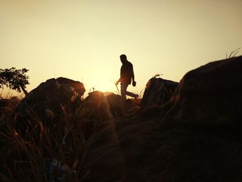 Rear view of silhouette man standing on rock against sky