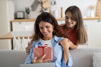 Portrait of smiling friends using phone while sitting on sofa at home