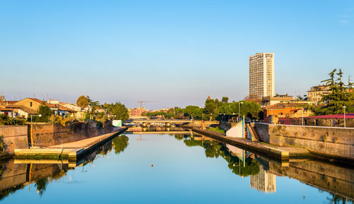 Reflection of buildings on river against clear sky