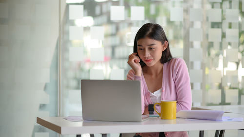 Young woman using phone while sitting on table