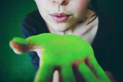 Close-up midsection of woman blowing on hand with green powder paint