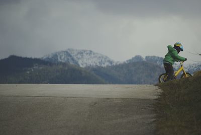 Boy riding bicycle on slope against mountain during winter