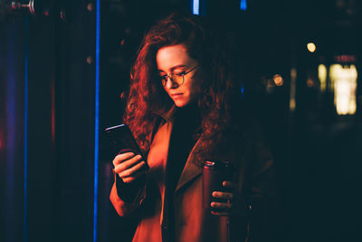 Young woman standing against illuminated nightclub