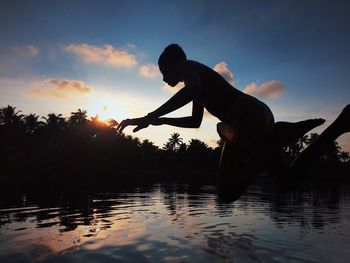 Silhouette man jumping in lake against sky during sunset