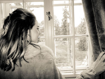 Side view of woman looking through window at home