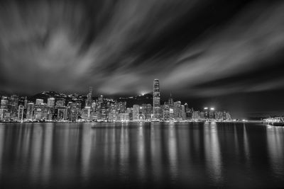 Illuminated city by sea against sky at night