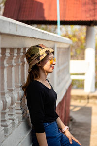 Side view of woman wearing sunglasses standing by wall