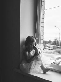 Full length of cute girl in costume sitting on window sill at home