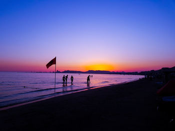 Silhouette people at beach against clear sky during sunset