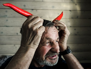 Close-up of senior man making horns with red chili peppers