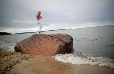Man standing on rock by sea against sky