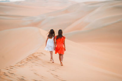 Rear view of women walking on sand dune