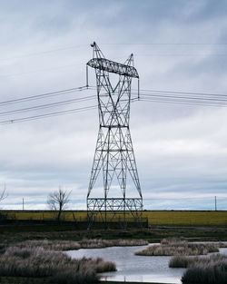 High voltage post or high voltage tower in the countryside with a small lake. cloudy background