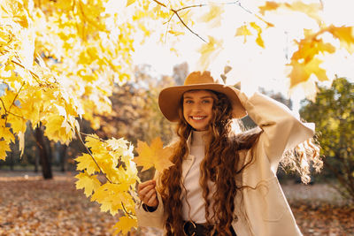 Portrait of young woman wearing hat standing against trees