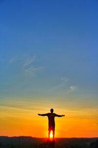 Silhouette man with arms outstretched standing against sky during sunset