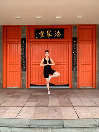 Full length portrait of young woman exercising by closed door