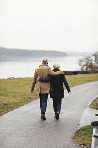 Rear view of senior couple with arm around walking on footpath during winter