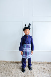 Portrait of cute boy wearing traditional clothing standing against wall