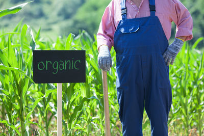 Midsection of farmer standing by sign at farm