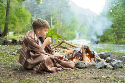Boy having tea while sitting near fire pit