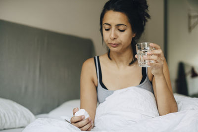Woman looking at pills while holding glass on bed