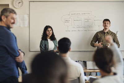 Male and female students interacting with friends during q and a session in classroom