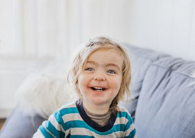 Portrait of smiling cute girl sitting on sofa at home
