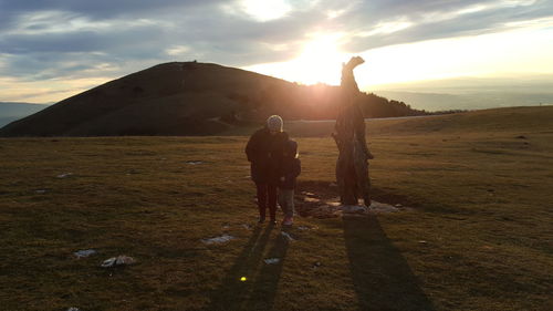 Rear view of people standing on land against sky during sunset