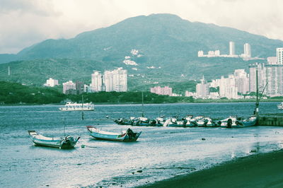 Boats moored on sea by city against sky