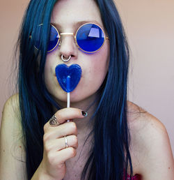 Young woman wearing blue sunglasses holding heart shape candy