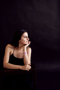 Portrait of young woman sitting against black background