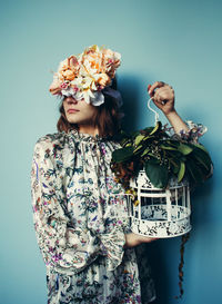 Woman holding birdcage while standing against blue wall