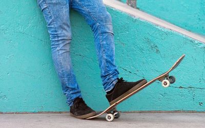 Low section of man with skateboard by wall