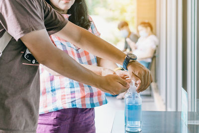 Midsection of woman holding glass while standing by window on table