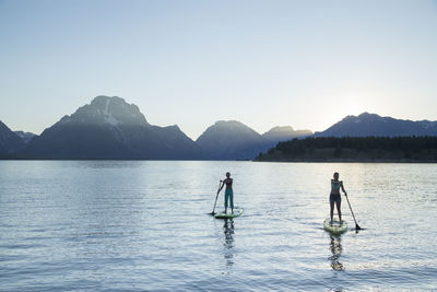 Female friends paddleboarding on lake against clear sky at grand teton national park