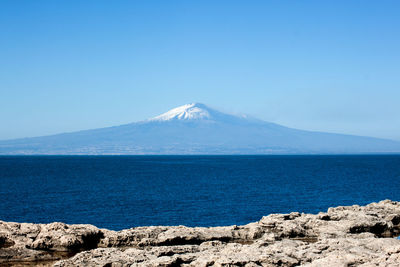 Scenic view of sea and mountains against clear blue sky