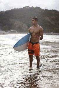 Thoughtful disabled man carrying surfboard while standing on shore